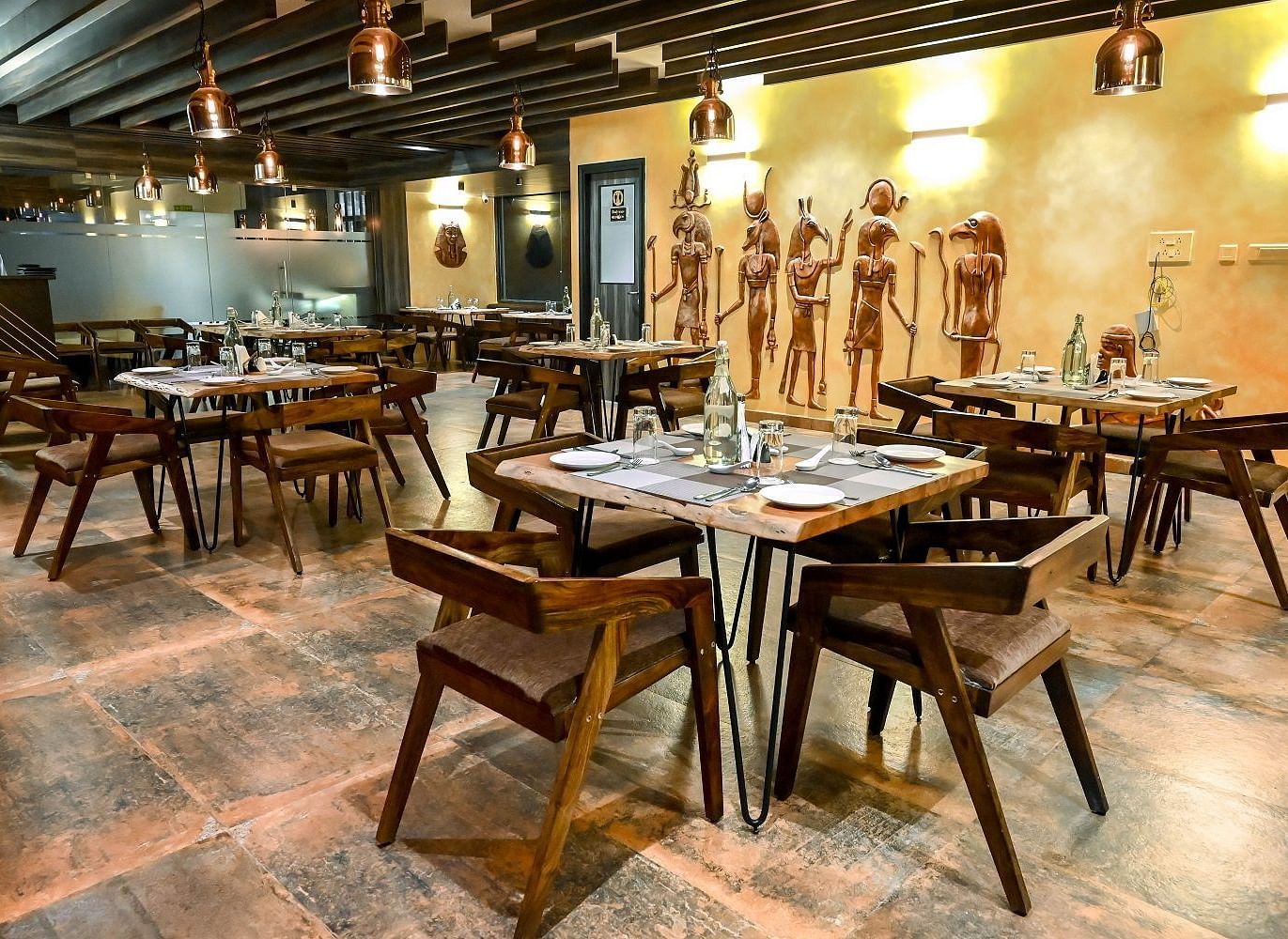Another angle of the restaurant dining space, focusing on a few tables set with placemats and cutlery, against a backdrop of unique wall art - Sea Hills Hotels, Sri Vijaya Puram (Port Blair)