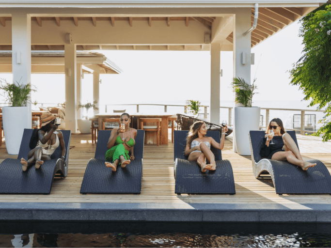 People are relaxing on lounge chairs under a covered outdoor area overlooking a serene view.
