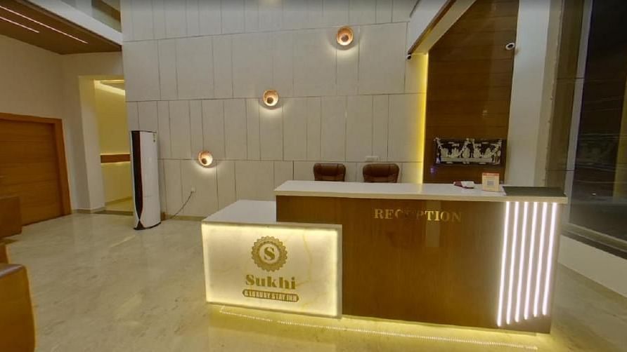 Reception area with a wooden desk featuring an illuminated logo, set against a backdrop of textured walls and ambient lighting.- Sukhi - A Luxury Stay Inn, Chikkamagaluru