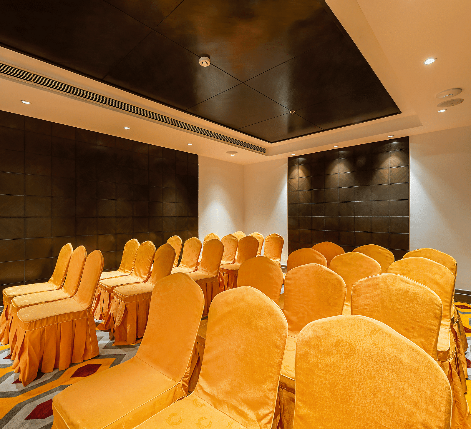 Conference room with yellow-orange chair covers, a dark tiled wall and a patterned carpet - TGI Grand Fortuna, Hosur