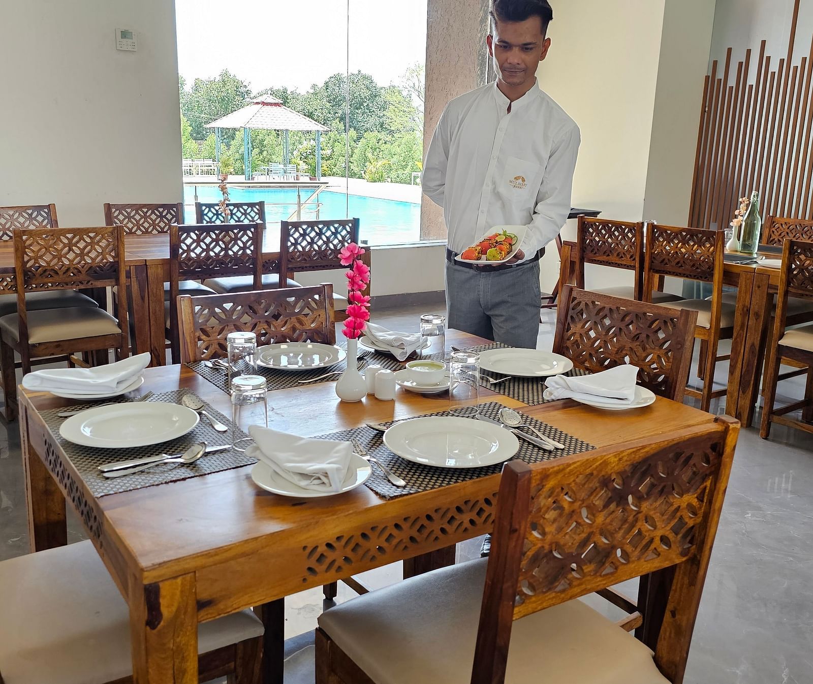 A man in a light-coloured shirt stands in a restaurant, possibly a waiter or staff member where tables and chairs are visible - Bamboo Saa Mulberry Resort, Pushkar