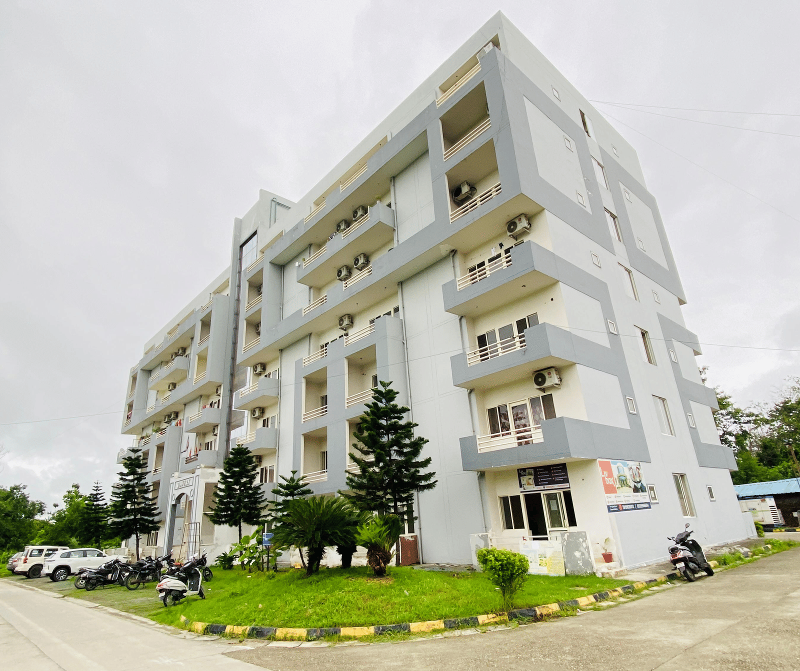The facade of multi-storey Livbox, Rudrapur featuring the balconies, greenery, and a curved driveway in the foreground.