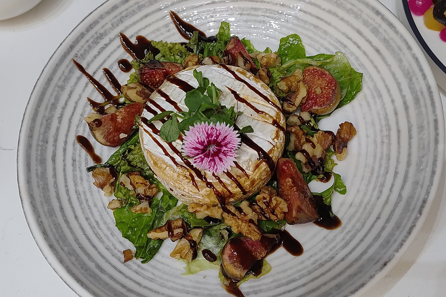 A food item garnished with leafy vegetable, herbs, other vegetables, flower, and sauce at The Wild Fork restaurant in La Marvella, Bengaluru.