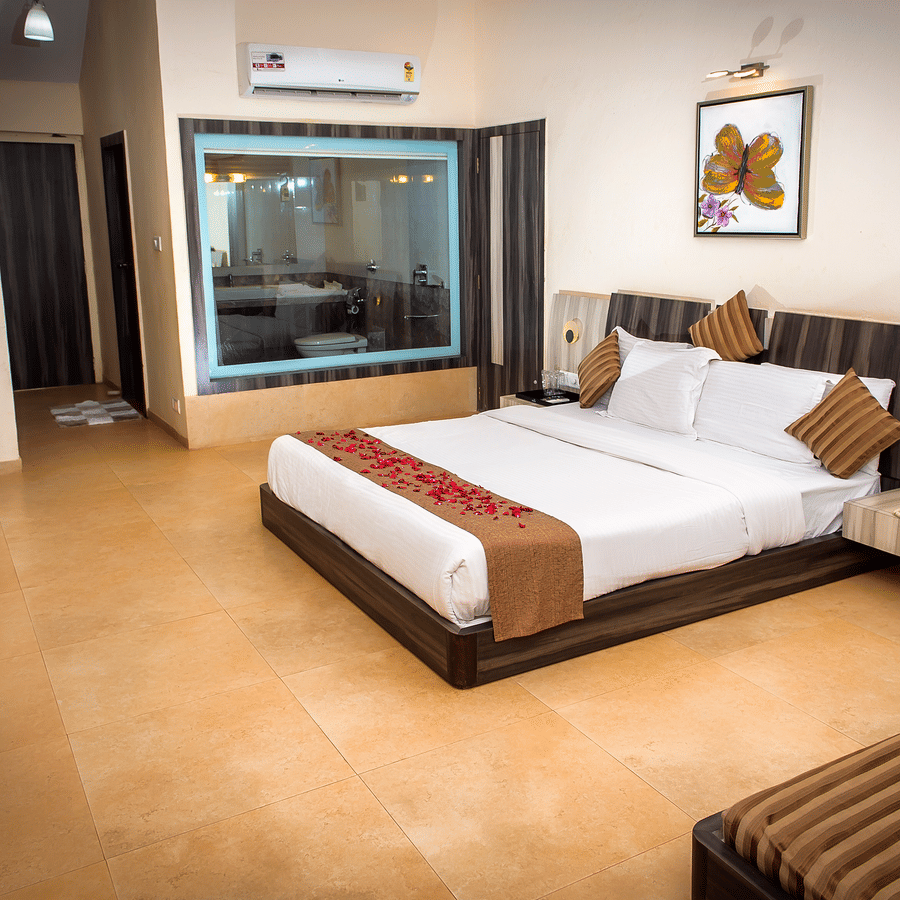 A view of the bed in Regency Room with its two side tables, glass window to the bathroom, diwan, and a consoel.