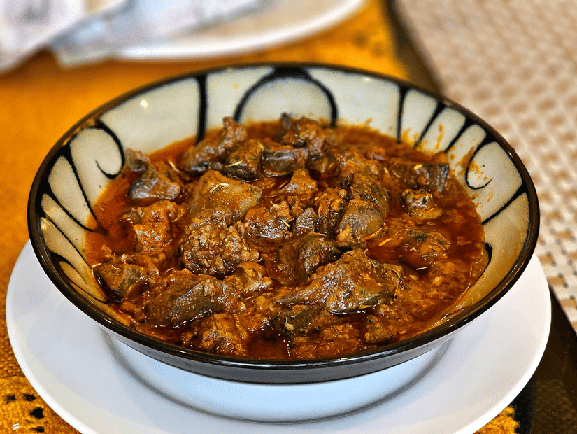 A serving of pork curry in a porcelain bowl kept on a plate.