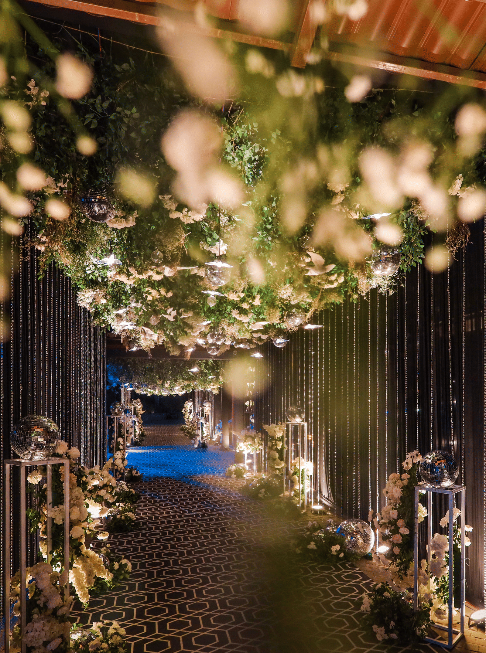 A luxurious, dimly lit hallway at Ananta Spa & Resort, Jaipur, features a thick floral and foliage ceiling canopy with warm string lights.