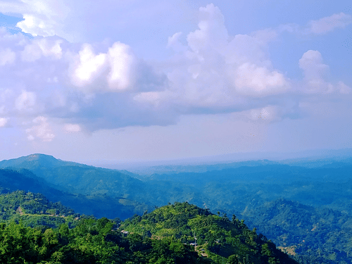 An overview of lush green mountains with white clouds on blue sky in the background.