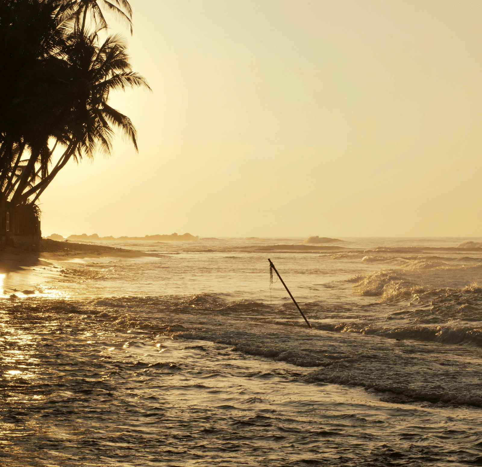 A beach at sunset with waves gently rolling onto the shore and a reflection of the sun on the water.