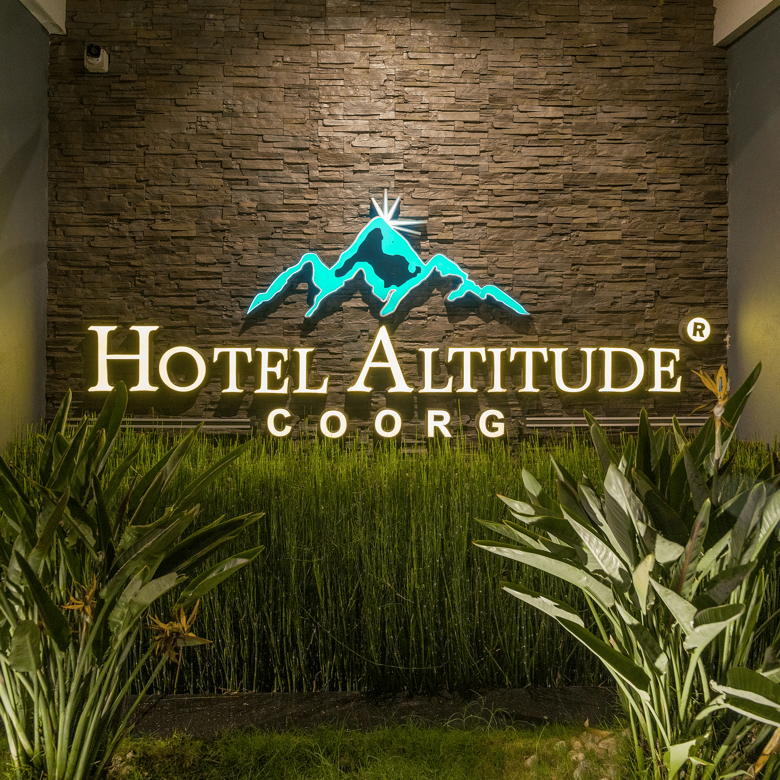 A wall with Hotel Altitude written on it and with plants in front at Hotel Altitude, Madikeri.