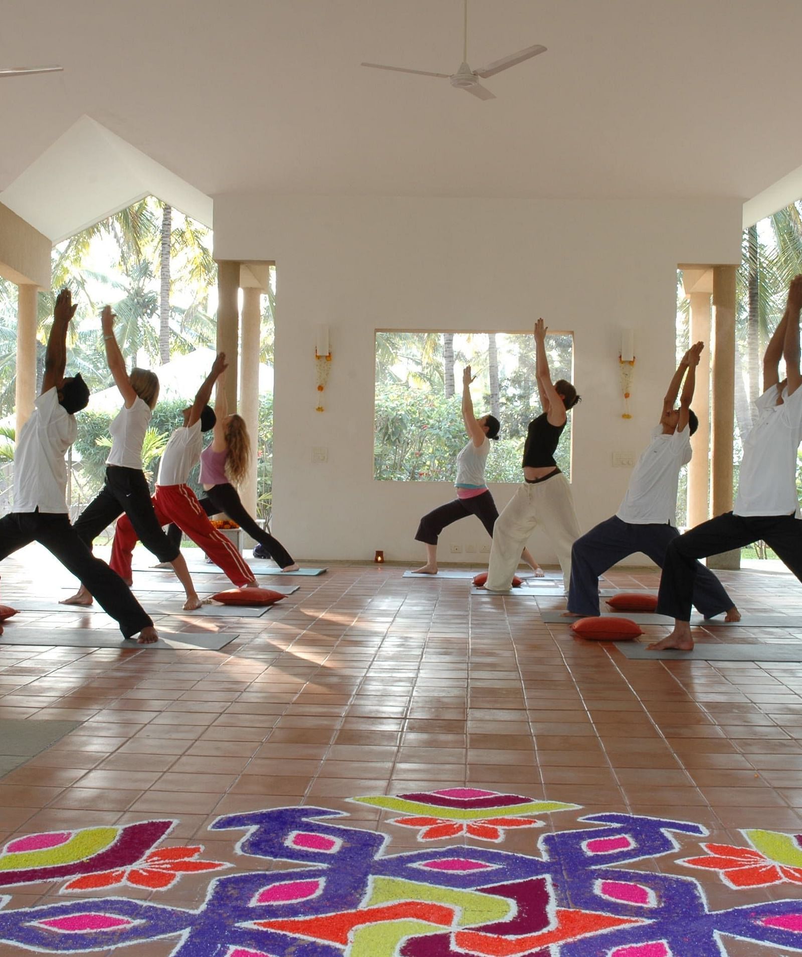People doing yoga poses in a bright room, colorful rangoli on floor - Shreyas Retreat