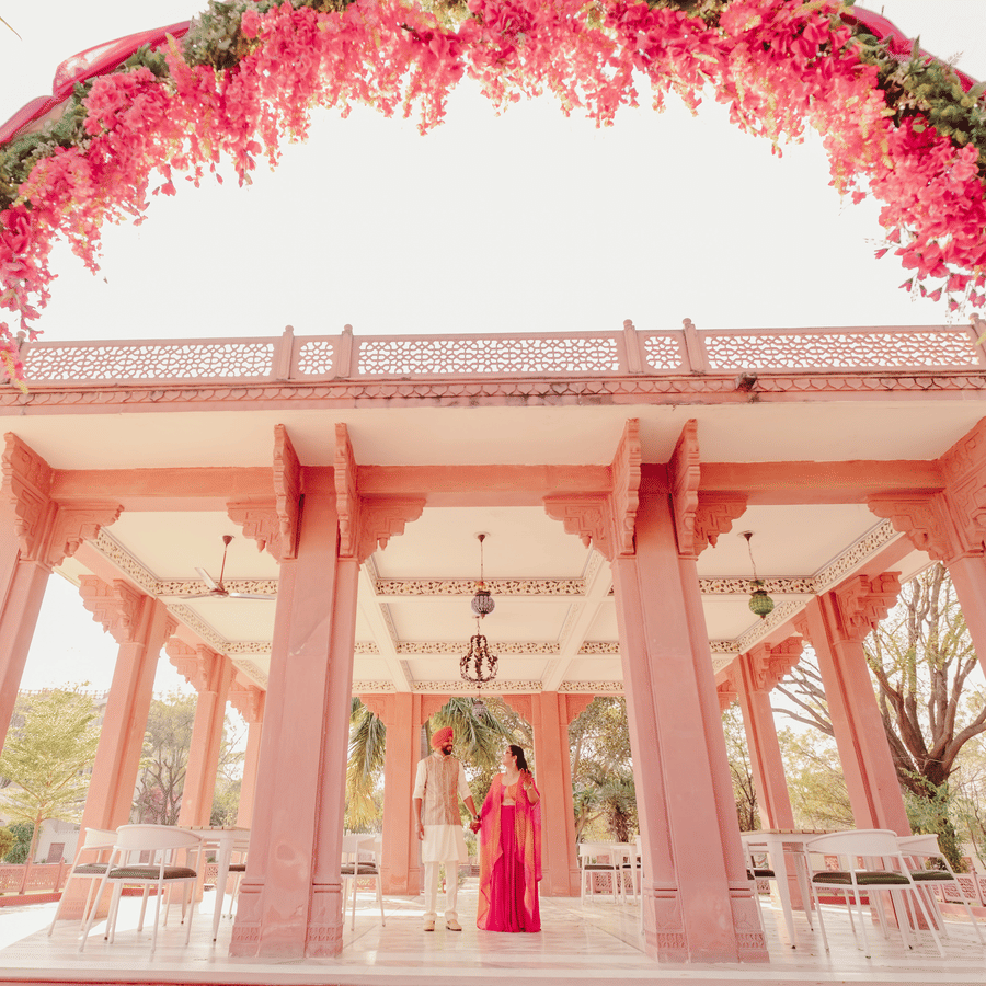 Jaswinder and Ritika standing beneath vibrant floral arch in outdoor pavilion at Umaid Palace wedding ceremony.