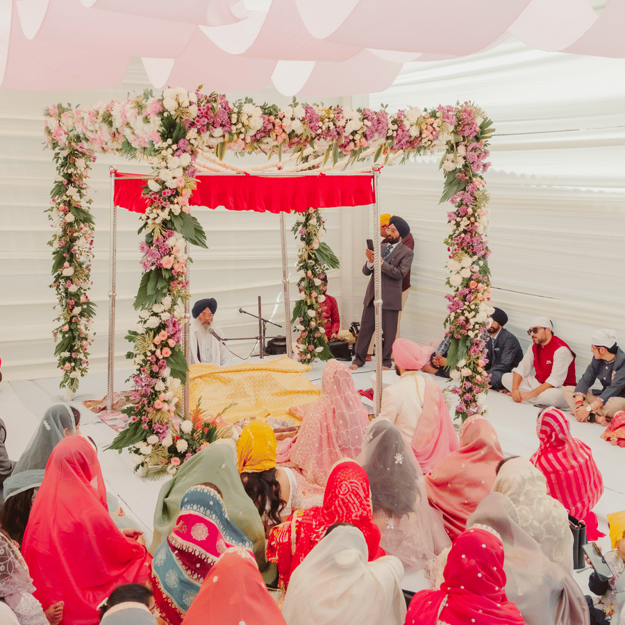 A wide view of an outdoor Anand Karaj wedding ceremony under a white canopy with guests seated on the floor facing a floral mandap at Umaid Palace.