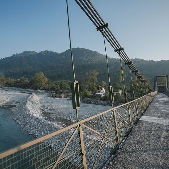 A suspension bridge over a river, with mountains in the background, daytime setting.