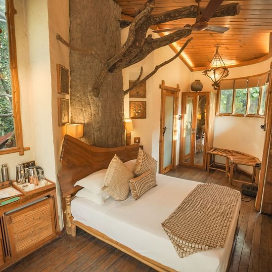 A bedroom with a bed, a lamp, and warm lighting, interior setting with wooden elements and large windows - The Den Corbett Resort & Spa, Kumeria.