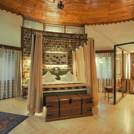 A bedroom with a wooden bed frame, a patterned rug, and warm lighting - The Den Corbett Resort & Spa, Kumeria.