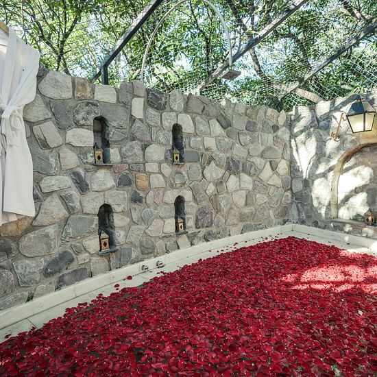 An outdoor stone wall with white fabric hanging and red rose petals on the ground - The Den Corbett Resort & Spa, Kumeria.