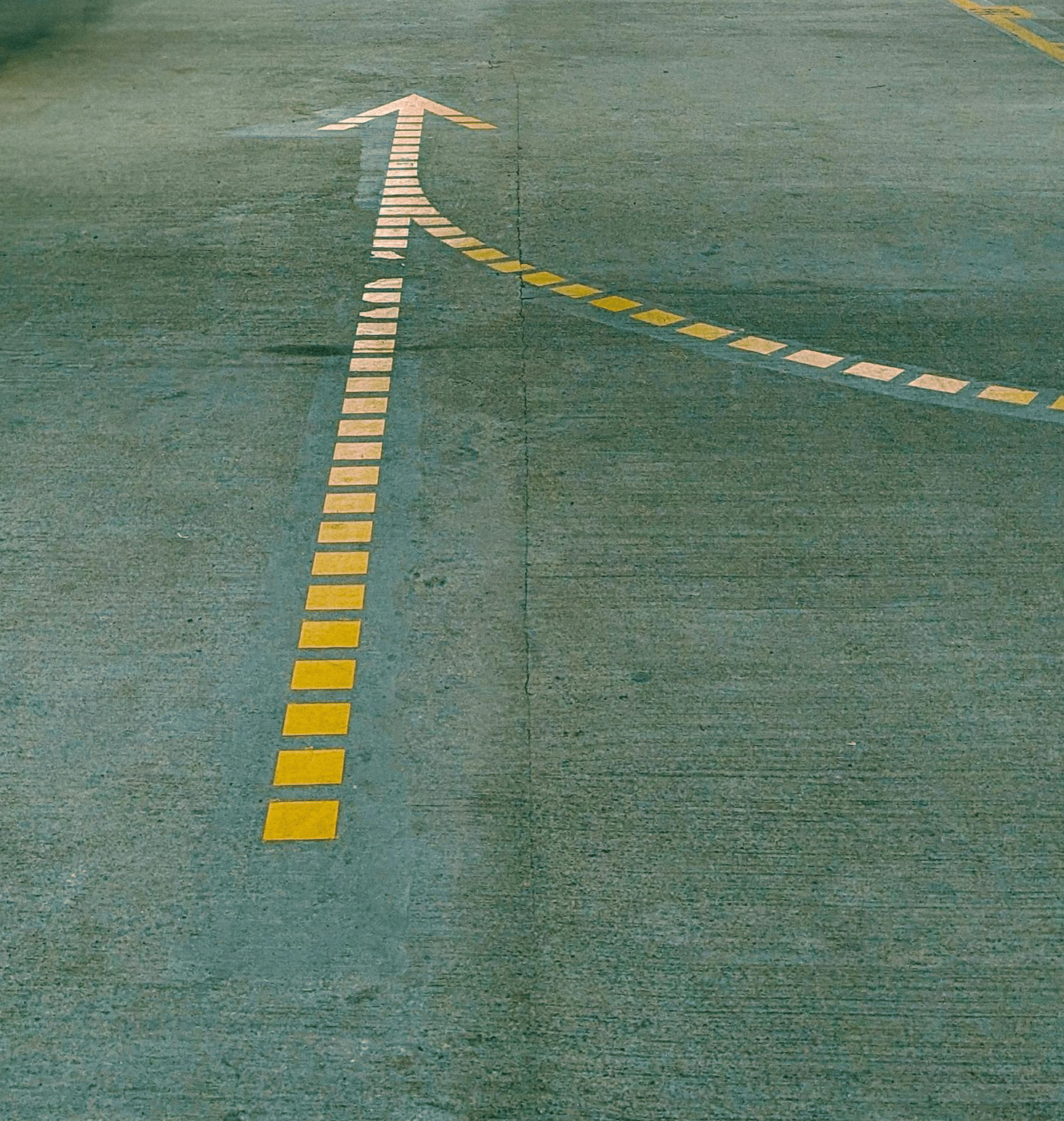 A low-light underground car park with yellow painted lines and a single white arrow on the concrete floor.