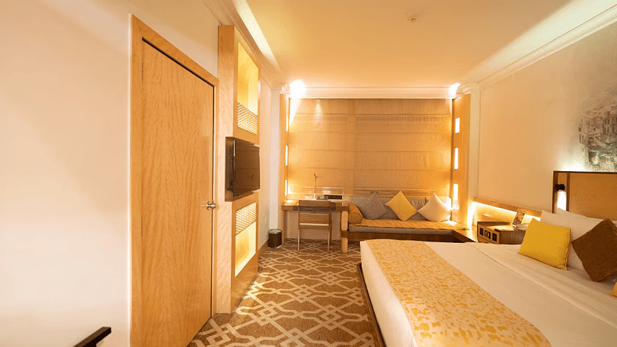 Deluxe room at Marco Polo Hotel, Dubai, featuring a king size bed, cushioned seating area, work desk and large windows.