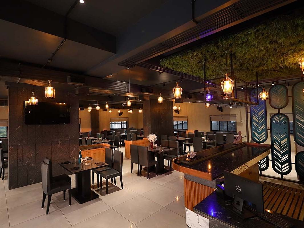 The image captures the ambiance of a restaurant featuring tables, chairs, a bar area, and decorative lighting - Lords Eco Inn Navsari.
