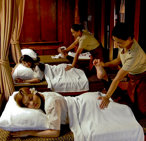 Two clients being massaged while resting their head on soft pillows, by two masseuses