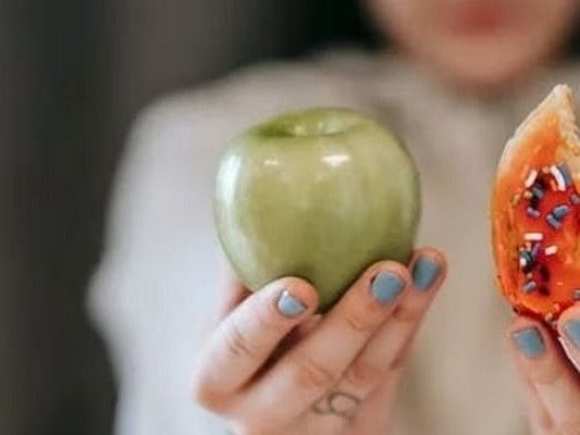a woman holding an apple in one hand and a doughnut in the other