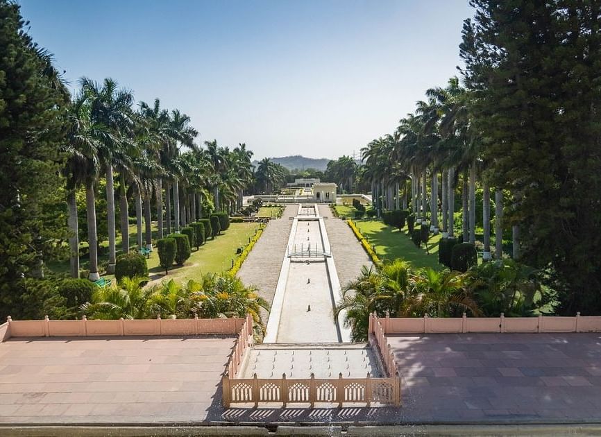 A scenic view of a garden with a long, winding pathway lined with trees and bushes. The garden is well-maintained and has a peaceful atmosphere.