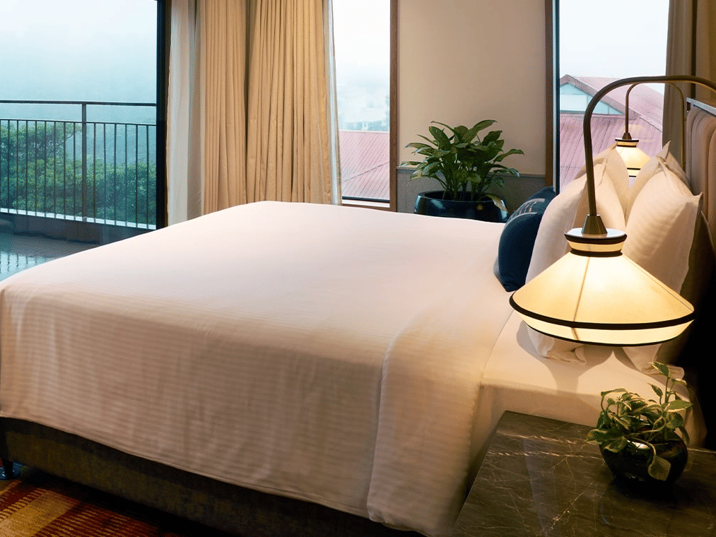 The hotel room with a large white bed, modern lamp, and full-length glass doors opening onto a balcony in the mist.