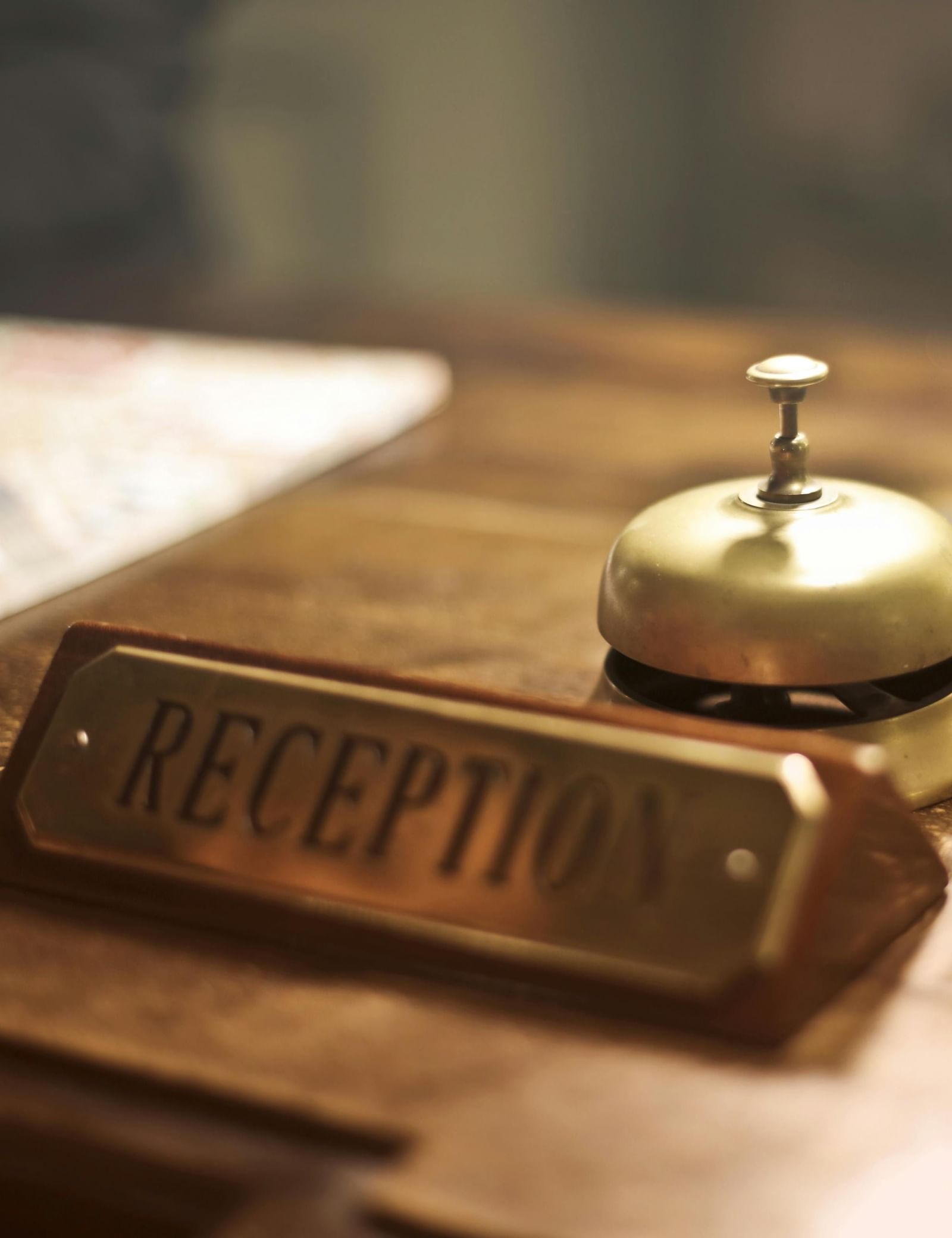 Close-up of a hotel reception desk with a brass bell, a “Reception” sign, and room keys on the counter.