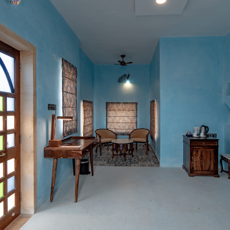An image of an indoor seating area with chairs and tables along with a work desk and table at a corner where  tea and coffee maker is kept - Karwaan Jaisalmer