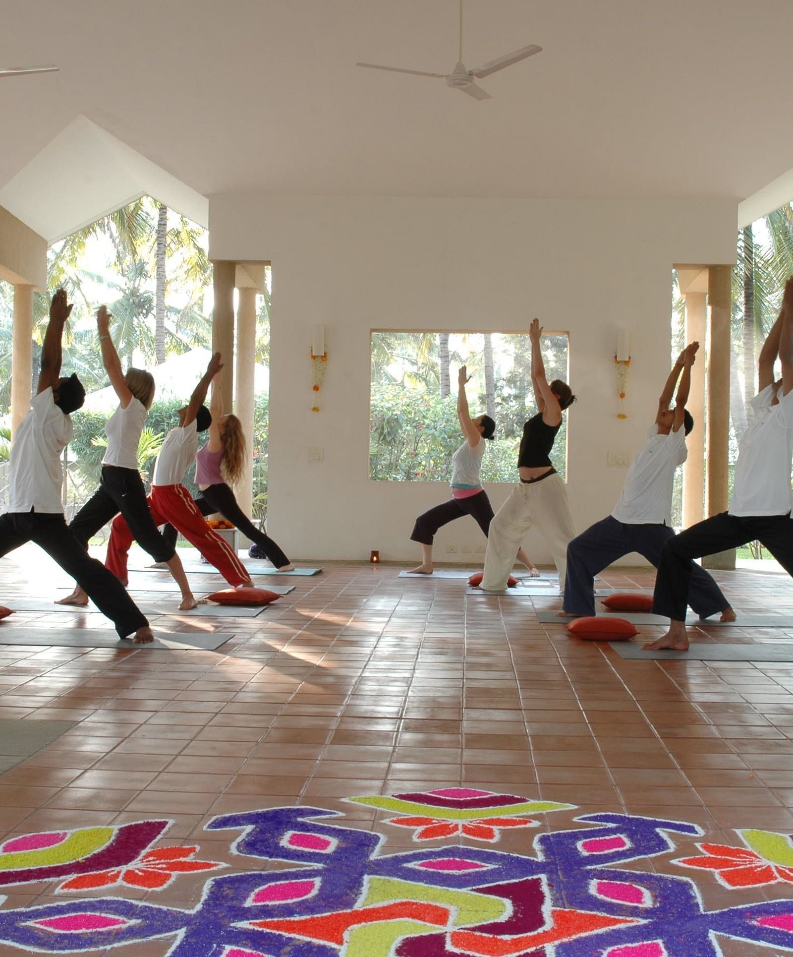 People doing yoga poses in a bright room, colorful rangoli on floor - Shreyas Retreat