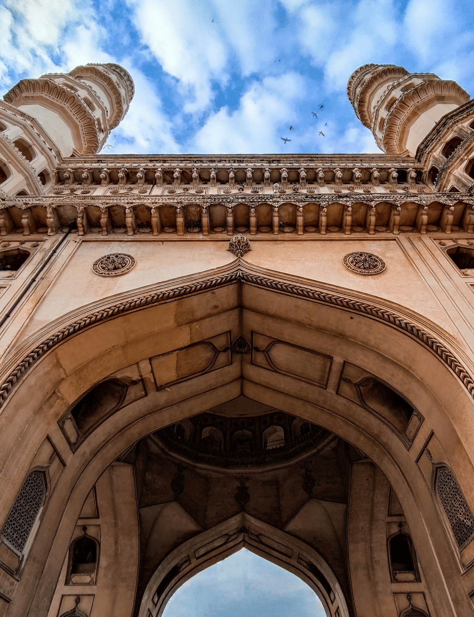 Close-up view of intricate archways and carvings on Charminar beneath a cloudy sky.