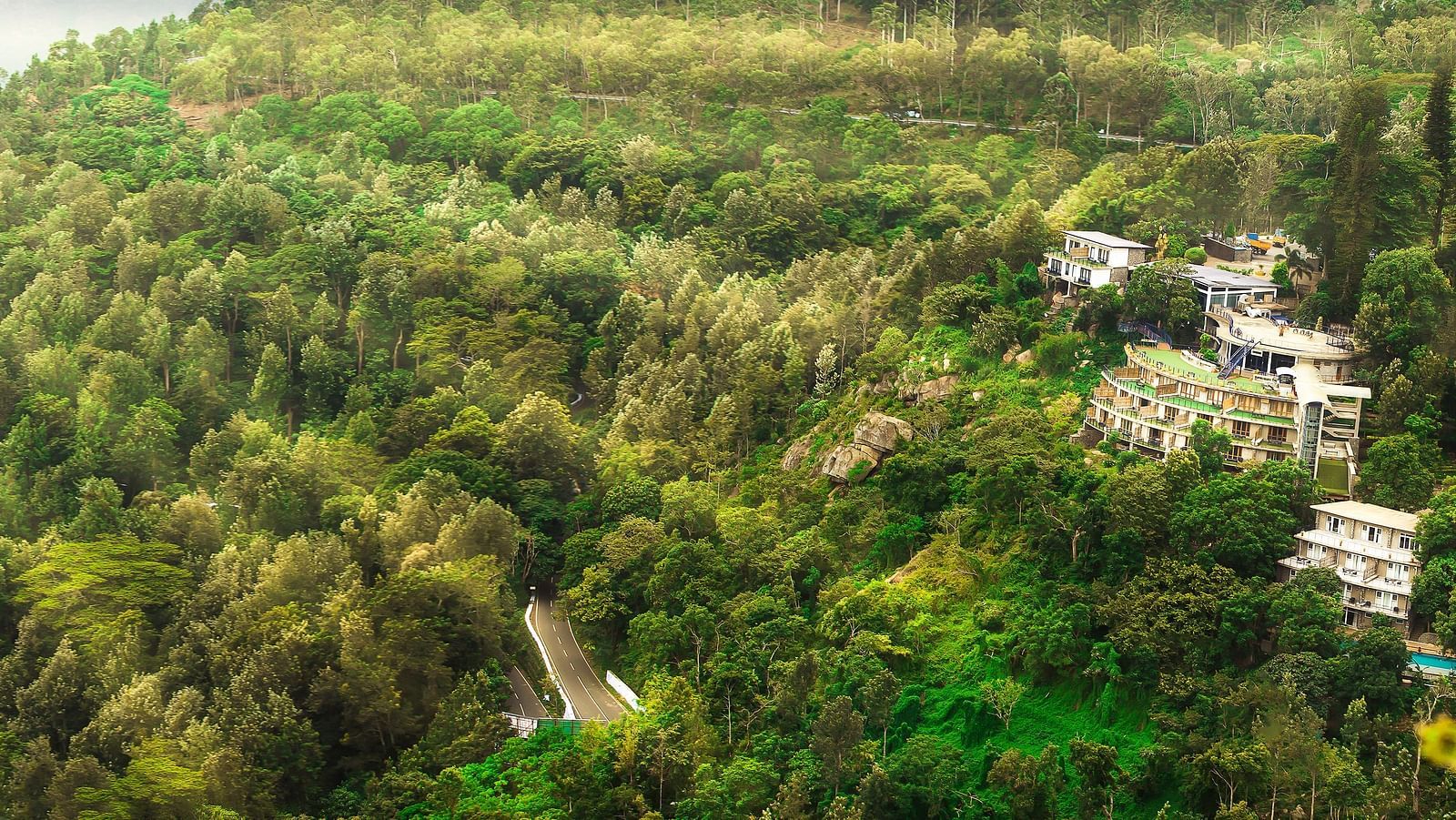 Drone shot of the hotel surrounded by mountains with sun light hitting the lush greenery - Great Trails Yercaud by GRT Hotels
