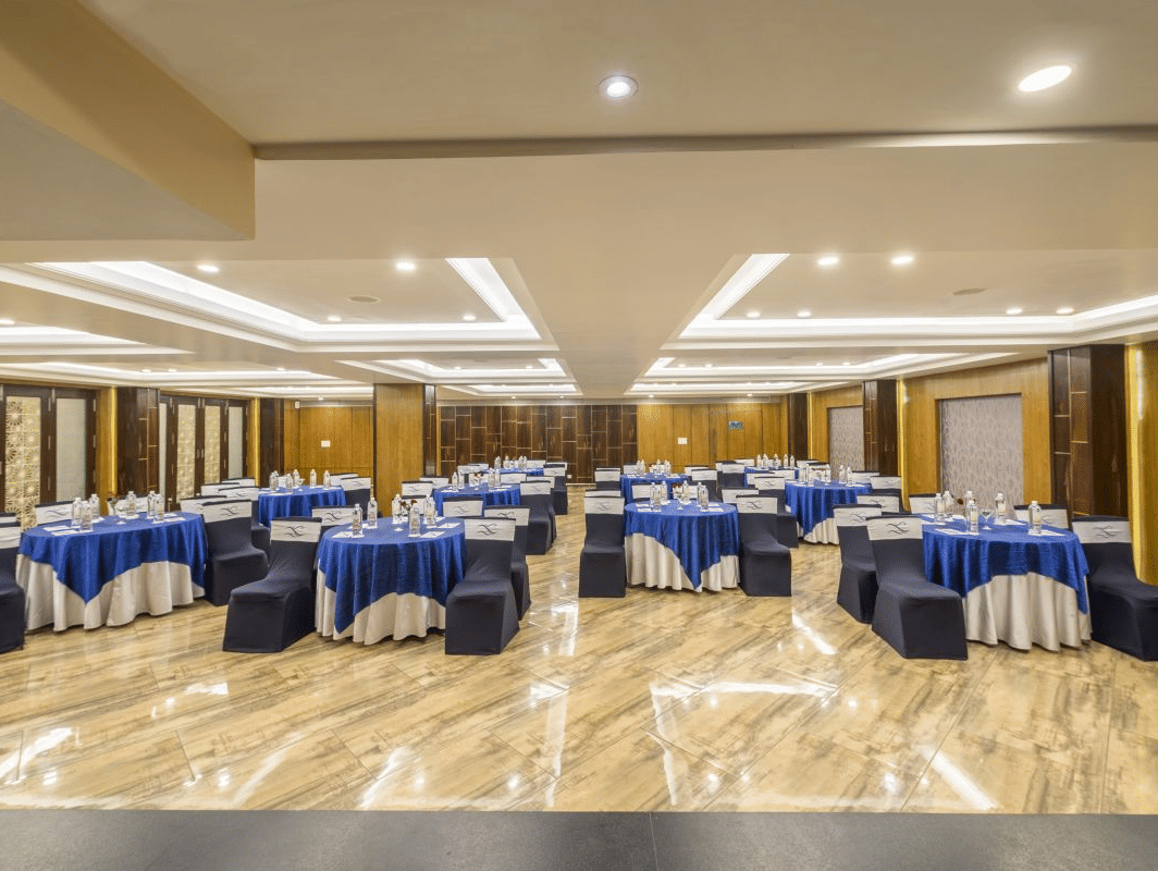 A well-lit conference room at The Citrine with blue and white tablecloths, chairs, and a stage setup.