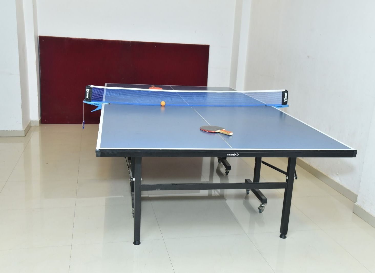 A table tennis setup in an indoor room with a table, net, two paddles, and a ball placed on it, at Highland Resort.