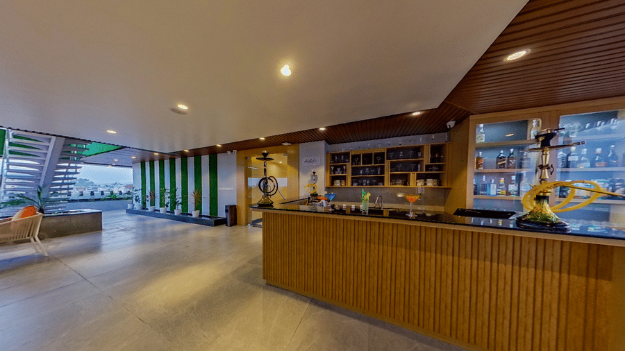 A wide view of Distil bar featuring an open space in the centre and a wooden panelled bar counter with assorted liquor bottles and a hookah stand | Lords CBC Plaza, Chitwan