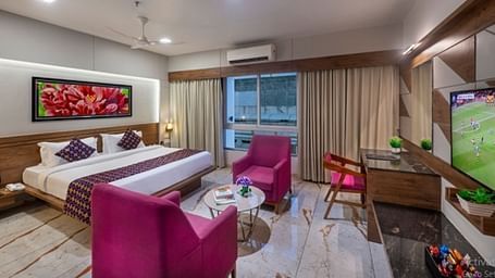 A room featuring a bed, a seating area with armchairs, and a television at Angel Lords Eco Inn Amreli.