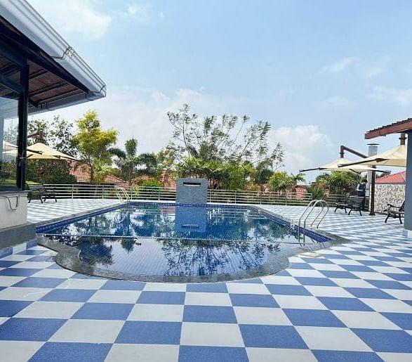A serene pool area at Woodstock Resorts, Coorg featuring a checkered tile pattern and surrounding greenery.