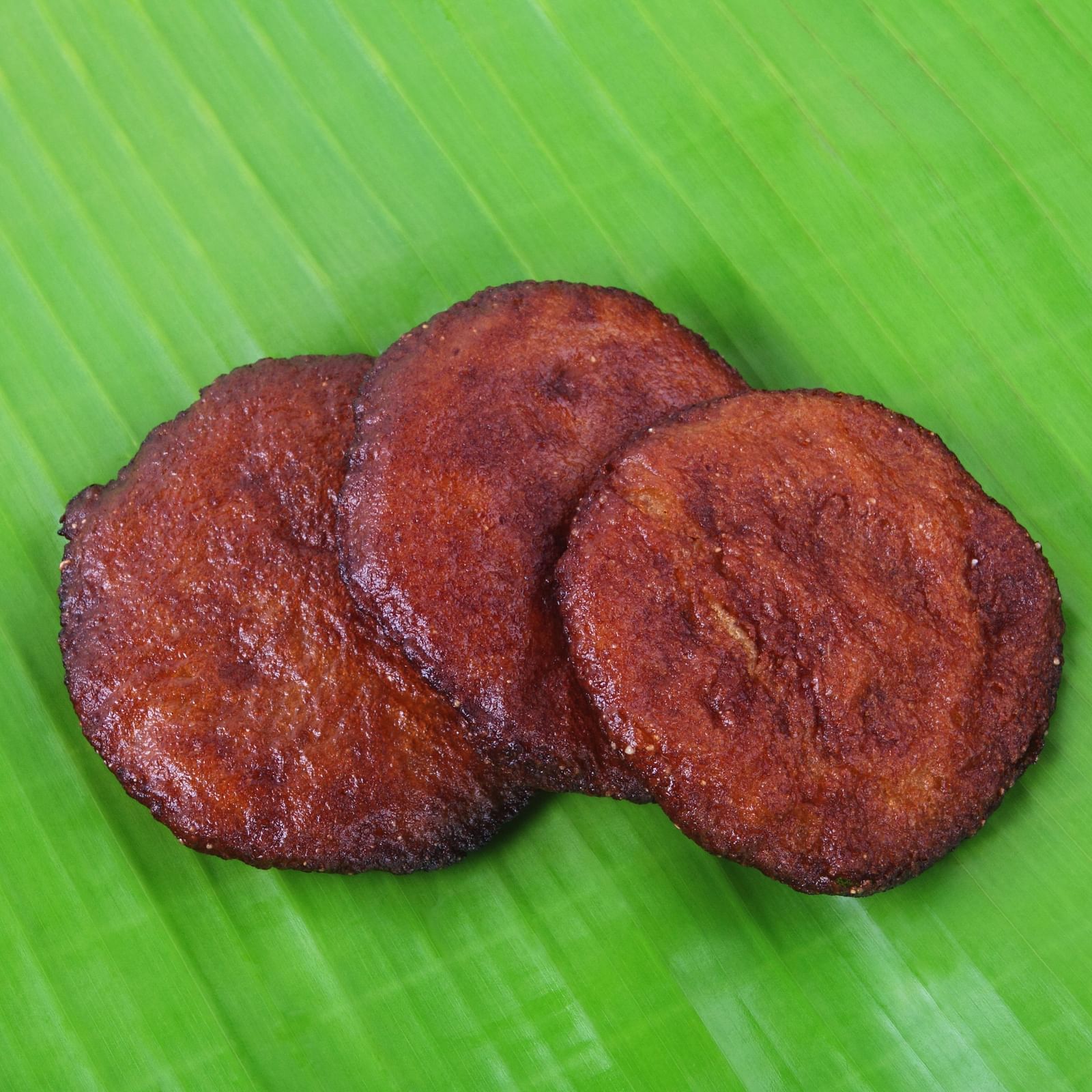 Three round, deep-fried plantain fritters neatly arranged on a vibrant green banana leaf.