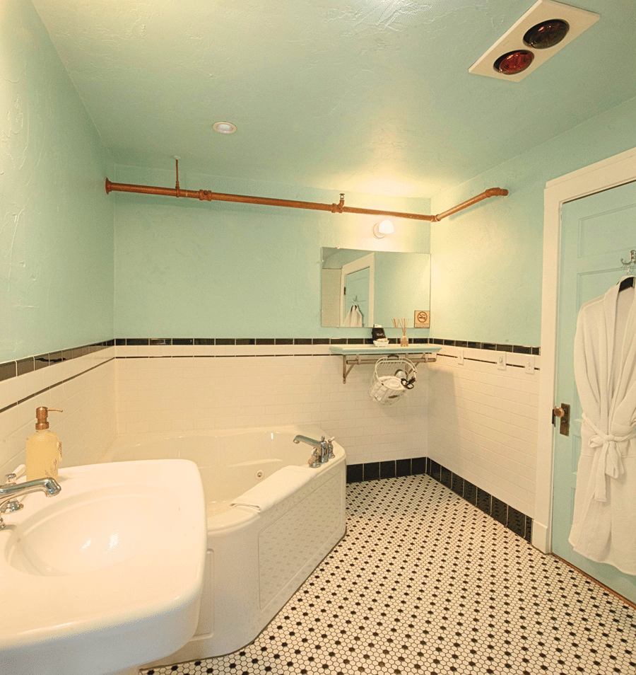 A mint green and white tiled bathroom with a clawfoot tub, wall-mounted sink, and decorative copper piping.
