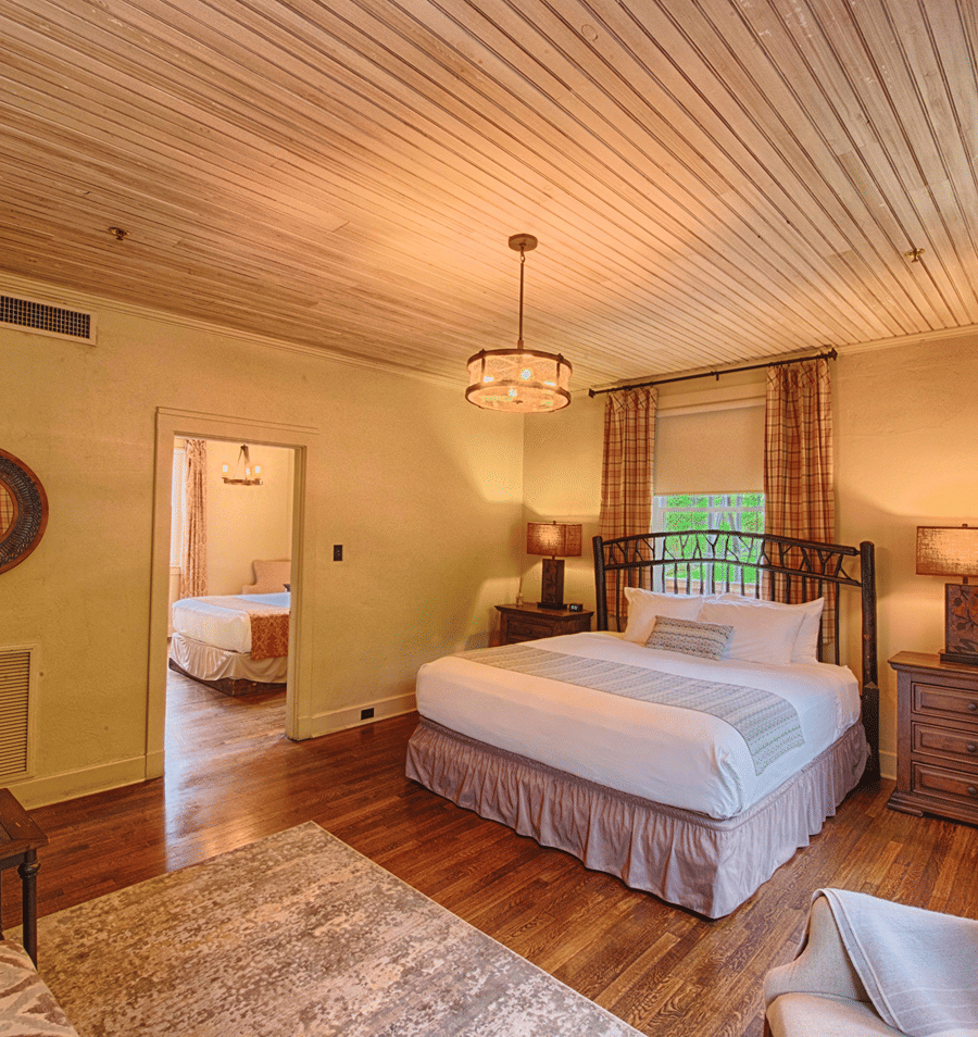 A wide view of a cozy guest room with a large bed, wooden floor, and wood-paneled ceiling.