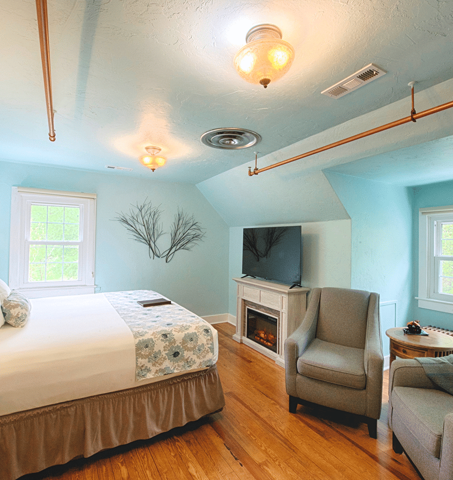 A wide view of a guest room with light blue walls, wood floors, and exposed copper piping.
