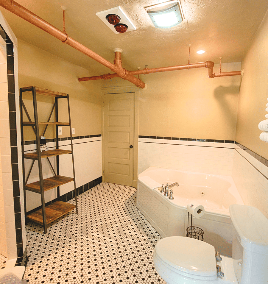 A bathroom with a bathtub, toilet, shelf, and exposed copper pipes.