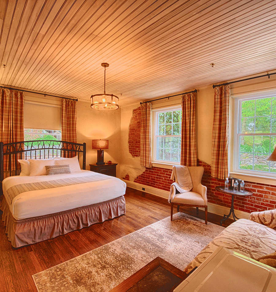 A wide view of a cozy guest room with a bed, chair, and window.