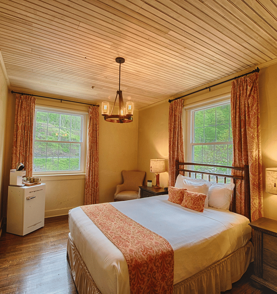 A wide view of a cozy guest room with a king-sized bed, wooden floor, and white ceiling.