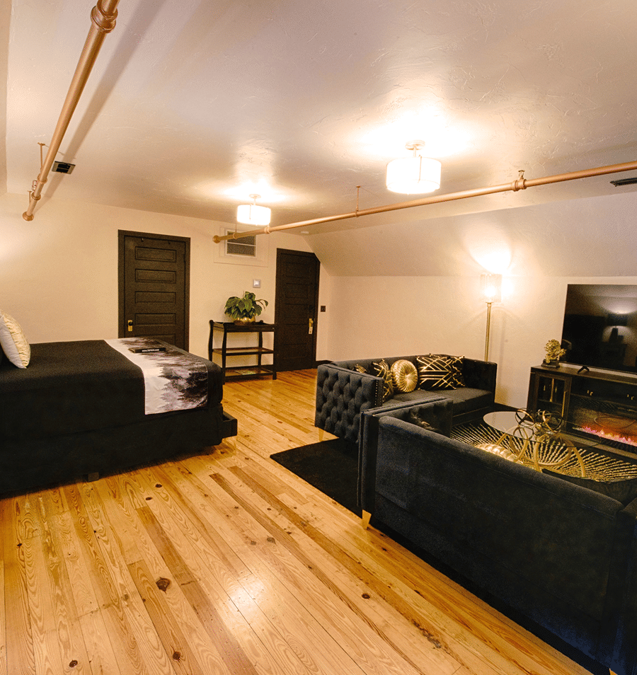 A wide-angle view of a hotel room with a bed, sofa, and fireplace.
