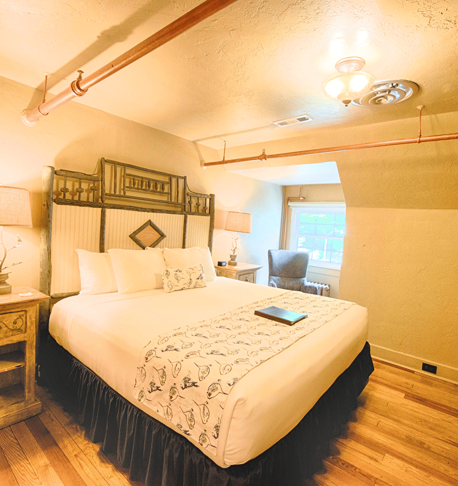A wide-angle view of a hotel room with a large bed, wooden nightstands, and a window.