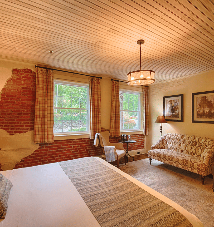 A wide view of a cozy guest room with a bed, sofa, and chair.
