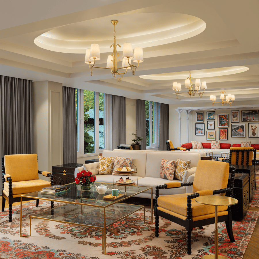 Spacious hotel lobby lounge with tiered tray snacks, yellow seating, and a gallery wall under warm recessed lighting.