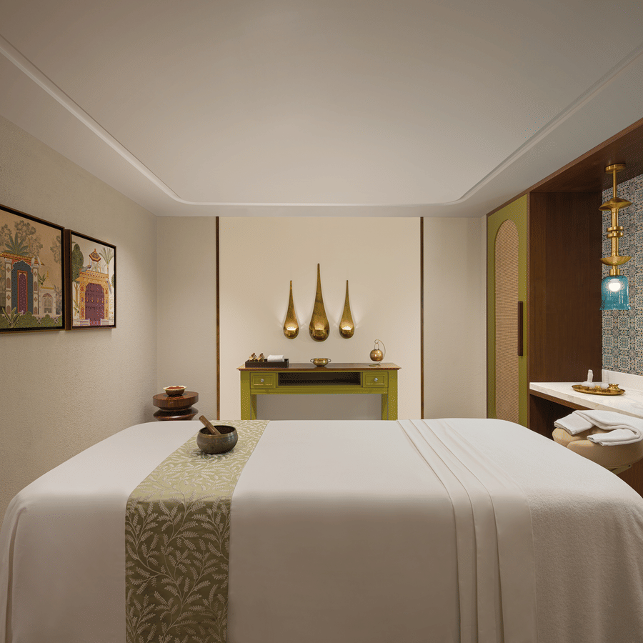 Single treatment room with a white massage bed, olive green accents, and gold teardrop wall art.