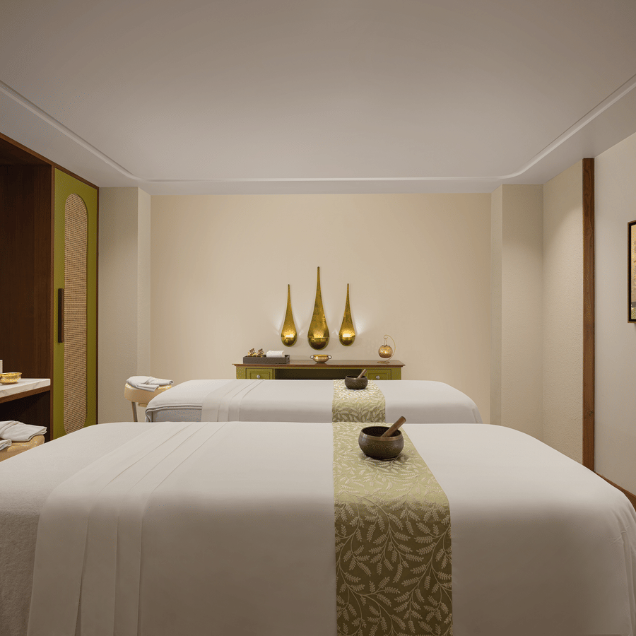 Relaxing spa room at Aloha on the Ganges Resort with two massage tables, patterned runners, warm lighting, decorative vases, pendant lights, and minimalist decor.